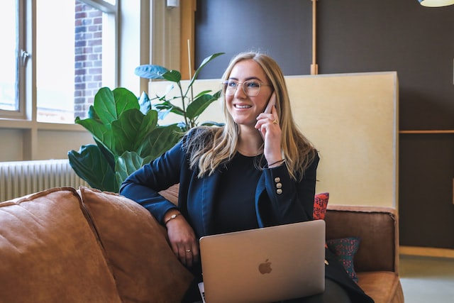 Person with blonde hair sitting on a leather couch talking on the phone